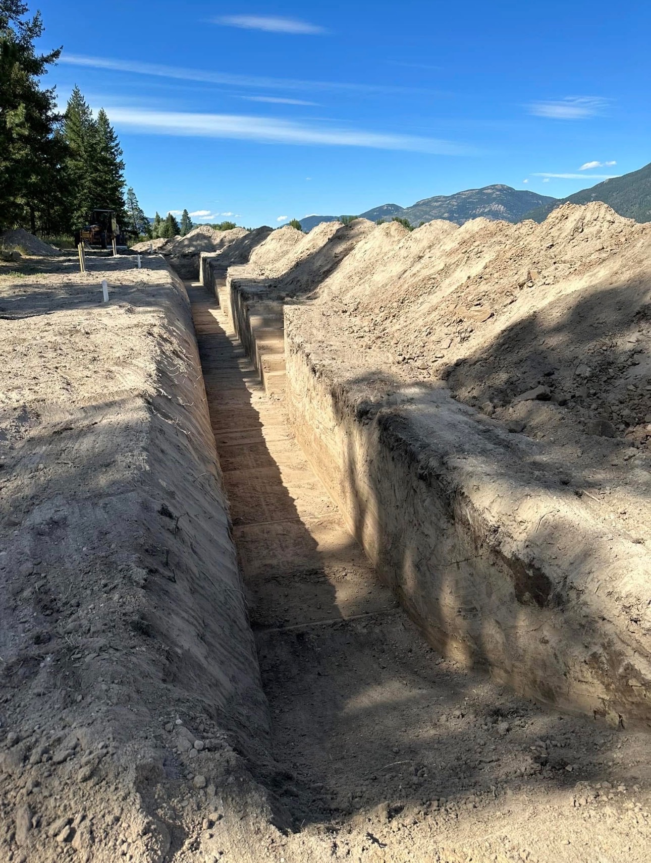 Deep, straight utility trench cut through sandy soil with mountains beyond