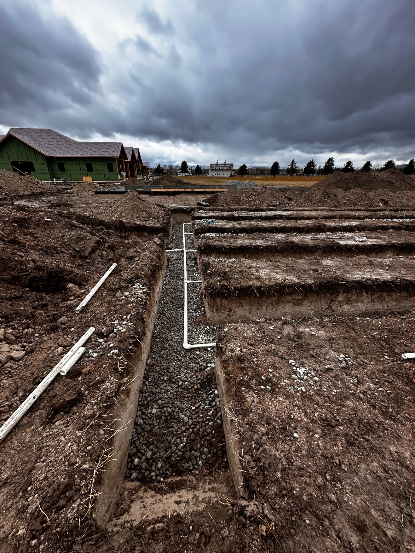Deep footing trench with gravel base under stormy Montana sky