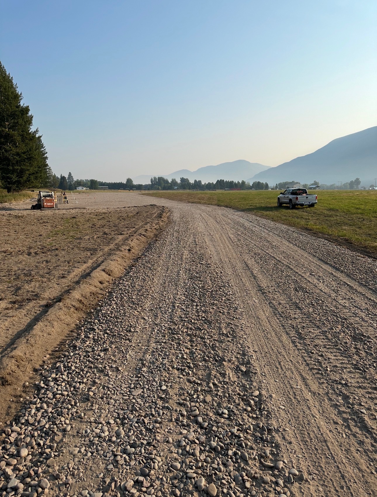 Fresh gravel driveway graded across a Montana field with mountains in the distance
