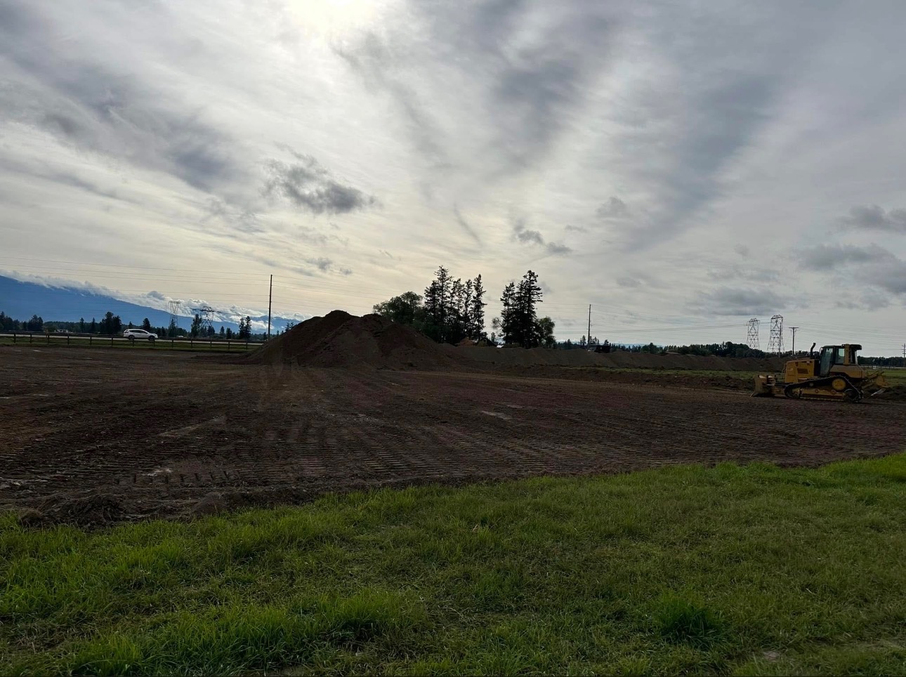 Freshly graded development site with bulldozer and topsoil piles under a wide Montana sky