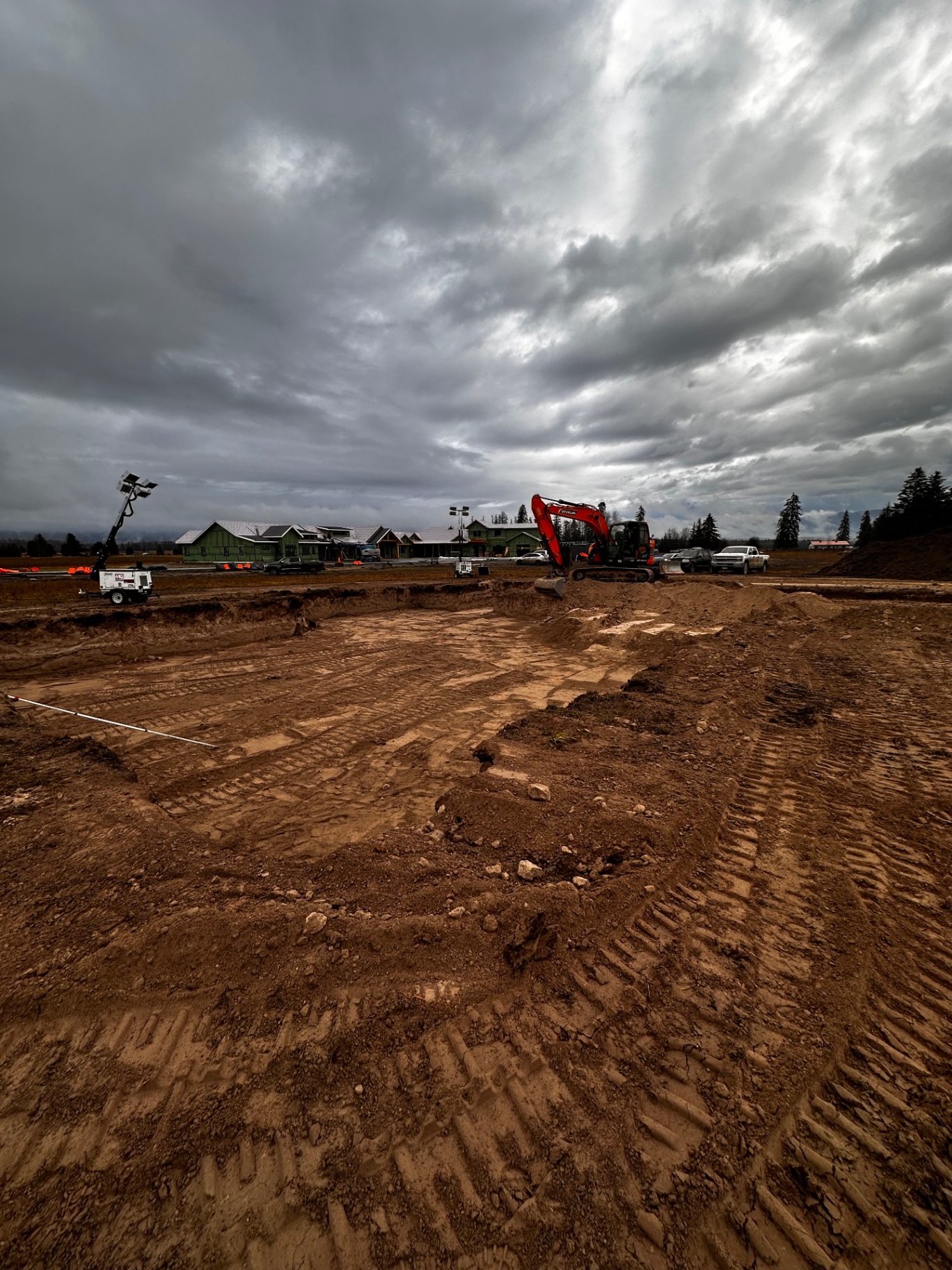 Site prep with excavator and light tower under cloudy sky